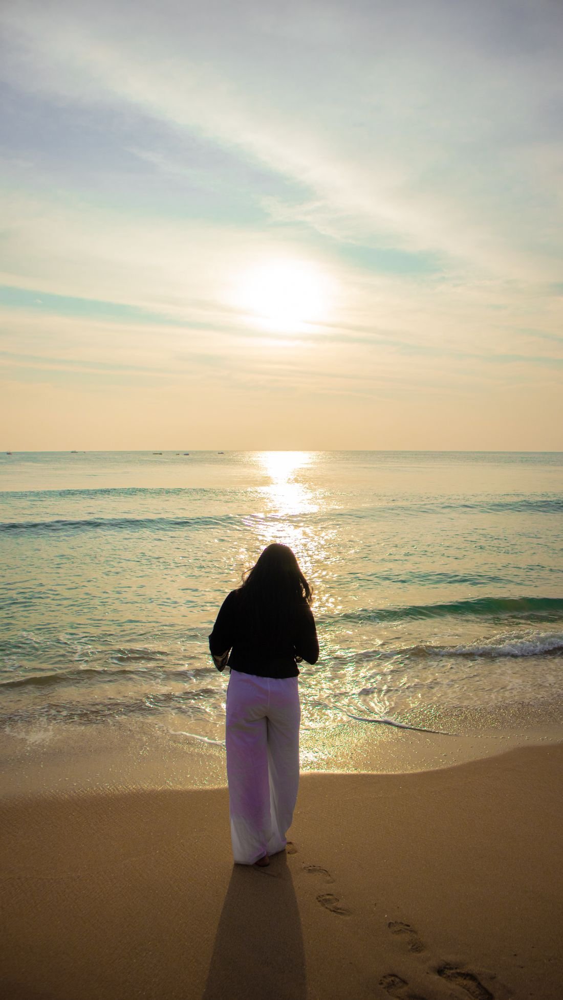 Une femme face à la mer au lever du soleil
